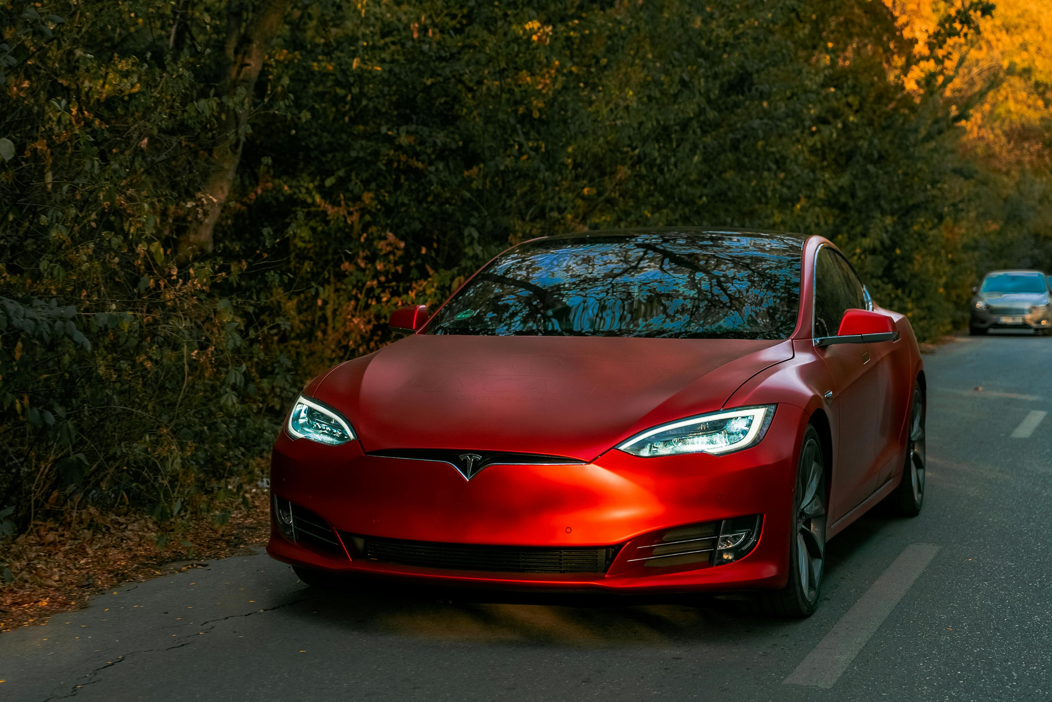 Red electric sedan driving on a tree-lined road